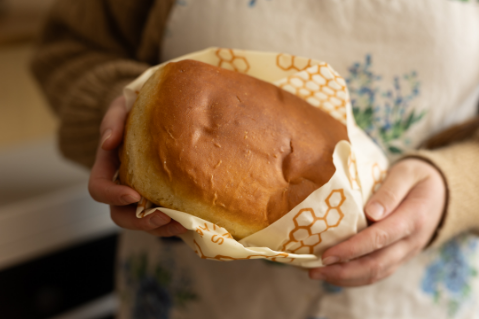 Person holding a loaf of bread wrapped in a decorative cloth with honeycomb patterns.