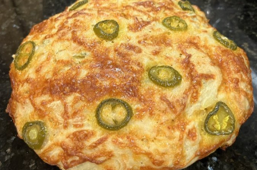 Round bread with a golden crust topped with jalapeño slices and melted cheese on a dark surface.